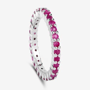 May include: A silver eternity band ring with a row of pink ruby gemstones.