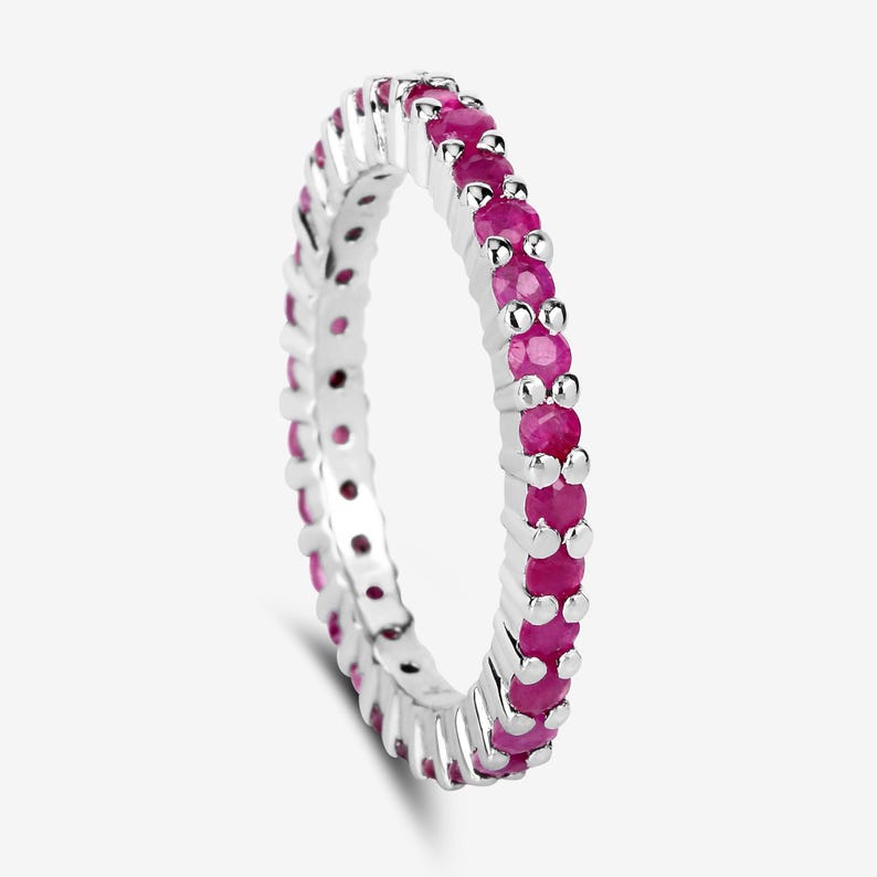 May include: A silver eternity band ring with a row of pink ruby gemstones.