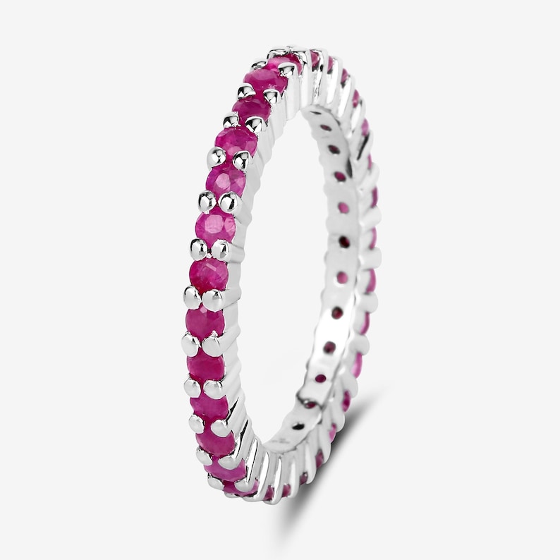 May include: A silver band ring with a row of pink gemstones around the entire band.