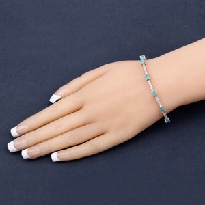 May include: A silver tennis bracelet featuring emerald green gemstones and small clear diamonds.