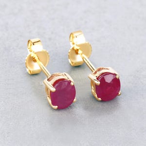 May include: A pair of gold stud earrings with round, red ruby gemstones.