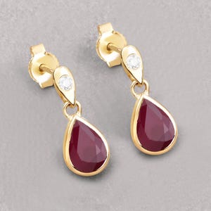 May include: A pair of gold earrings featuring a teardrop-shaped ruby gemstone and a small diamond accent.