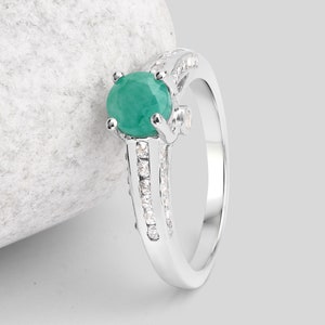 May include: A silver ring with a large green emerald gemstone and smaller clear gemstones set in the band.