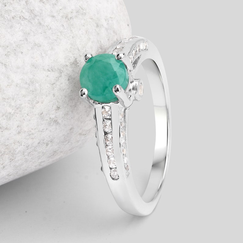 May include: A silver ring with a large green emerald gemstone and smaller clear gemstones set in the band.
