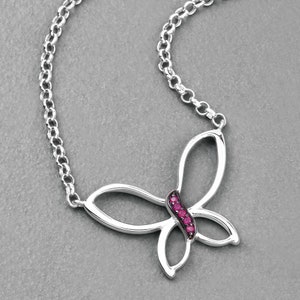May include: A silver-colored necklace featuring a butterfly pendant. The butterfly design has open wings and is accented with a row of small, vibrant red gemstones. The chain is a linked design.