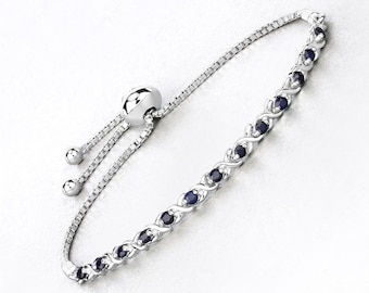 Op de afbeelding: Zilverkleurige armband met een rij donkerblauwe edelstenen in een afwisselend patroon. De armband heeft een fijne ketting en een schuifsluiting voor verstelbare maatvoering. De edelstenen zijn ovaal en gelijkmatig verdeeld.