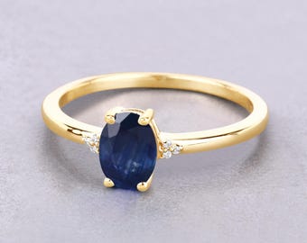 May include: A gold ring featuring a large, oval-cut, deep blue gemstone. Small, clear accent stones flank the main stone. The ring has a simple, polished band and a classic setting.
