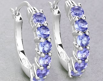May include: A pair of silver hoop earrings with a row of light blue gemstones. The earrings are made of metal and have a polished finish.