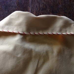 May include: Close-up of the back of a yellow shirt collar with a red and white zig-zag stitch detail.
