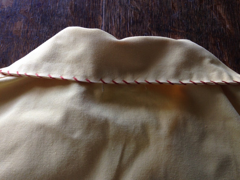 May include: Close-up of the back of a yellow shirt collar with a red and white zig-zag stitch detail.