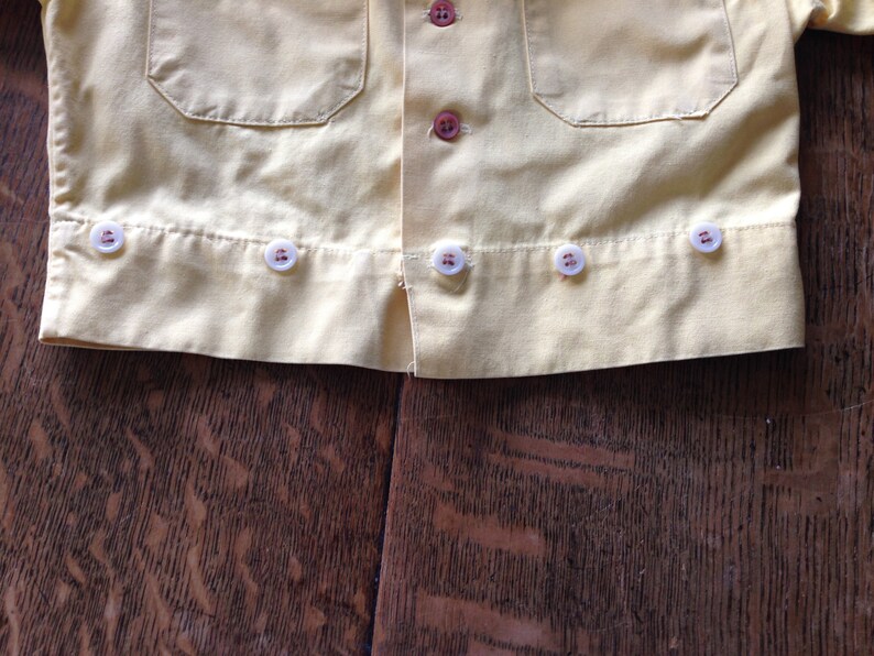May include: A yellow button-down shirt with white buttons. The shirt has a pocket on the left side and a row of buttons down the front.
