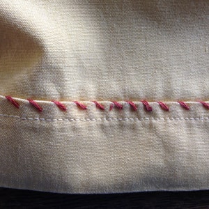 May include: Close-up of a yellow fabric with a red stitched seam. The fabric has a woven texture.