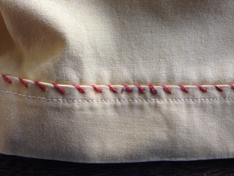 May include: Close-up of a yellow fabric with a red stitched seam. The fabric has a woven texture.