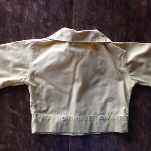 May include: A yellow short-sleeved shirt with a collar and two buttons on the bottom. The shirt has red stitching around the edges.