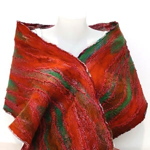 May include: A textured shawl featuring a vibrant pattern of diagonal stripes in shades of deep red, burnt orange, and forest green. The fabric has a thick, felted appearance with raised, wavy ridges running across the surface of the garment.