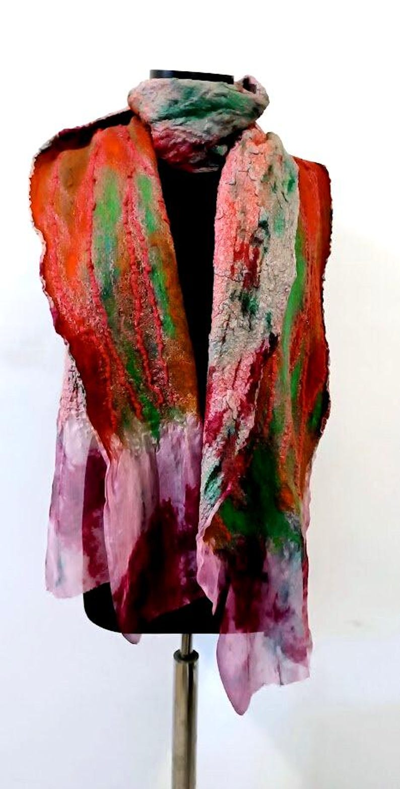 May include: A long, textured scarf featuring a vibrant blend of orange, green, and deep red felted wool fibers. The lower sections transition into a lighter, semi-sheer pink fabric with mottled, watercolor-like patterns and uneven, frayed edges.