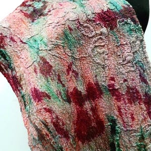 May include: A textured scarf featuring a mottled pattern of deep red, vibrant green, and soft peach tones. The fabric displays a dense, felted appearance with an uneven, organic surface structure that creates a multi-dimensional visual effect.