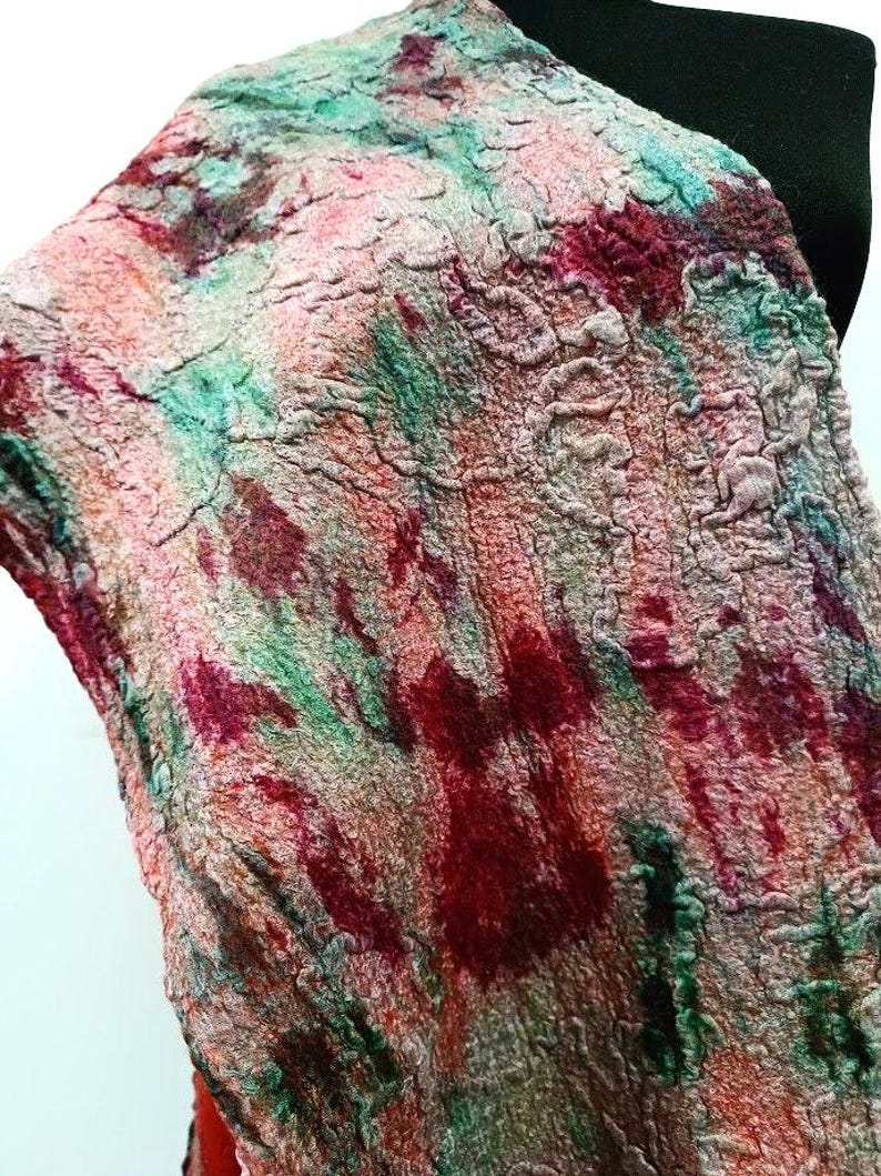 May include: A textured scarf featuring a mottled pattern of deep red, vibrant green, and soft peach tones. The fabric displays a dense, felted appearance with an uneven, organic surface structure that creates a multi-dimensional visual effect.