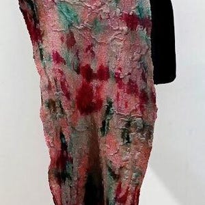May include: A long, textured scarf featuring a mottled pattern of pink, deep red, and teal green hues. The fabric has a felted, uneven surface with visible fibers and organic color blending, draped vertically over a black display form.