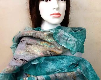 May include: A teal and gray felted wool scarf draped on a mannequin. The scarf features a blend of colors, including teal, gray, and hints of pink and brown. The scarf has a textured appearance with a flowing, layered design.
