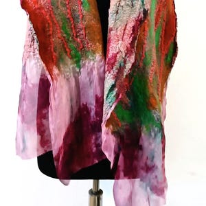May include: A scarf featuring a combination of felted wool and sheer silk fabric. The design displays a vibrant abstract pattern with bold streaks of red, bright green, and orange felted textures transitioning into a soft, flowing pink and purple silk.