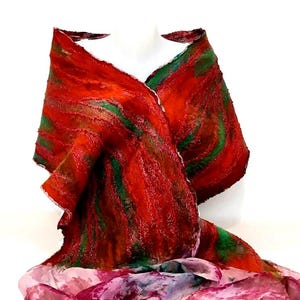 May include: A textured shawl featuring a vibrant blend of deep red and forest green fibers in a swirling pattern. The lower section transitions into a lighter, semi-sheer fabric with mottled shades of pink, purple, and white, creating a contrast.