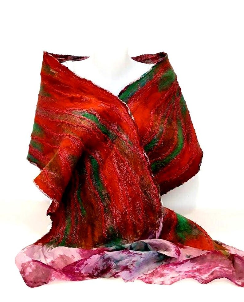 May include: A textured shawl featuring a vibrant blend of deep red and forest green fibers in a swirling pattern. The lower section transitions into a lighter, semi-sheer fabric with mottled shades of pink, purple, and white, creating a contrast.