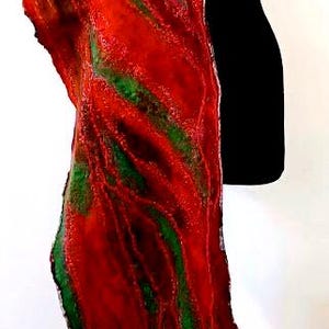 May include: A long, rectangular felted scarf featuring a vibrant, swirling pattern of deep red, bright orange, and forest green fibers. The textile has a textured, organic surface with uneven edges and a sheer, ruffled hem at the bottom end.