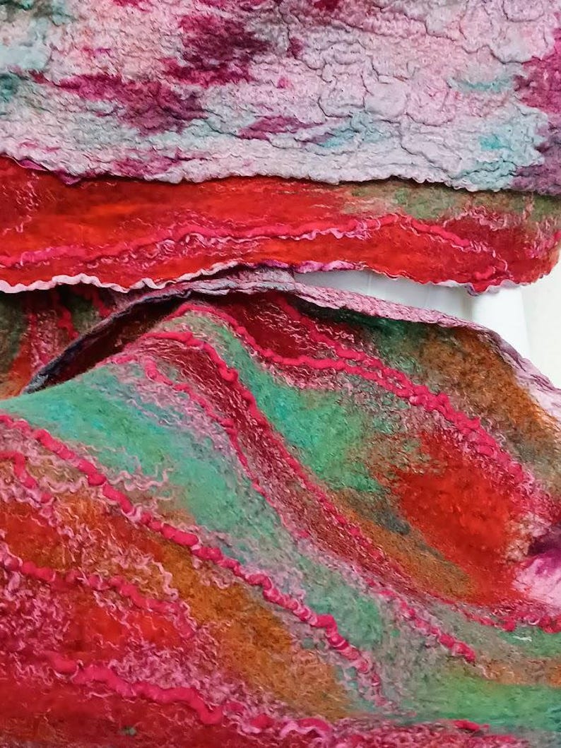 May include: A felted textile featuring a textured surface with layered colors including vibrant red, deep orange, teal green, and magenta. The material displays wavy, raised lines of fiber that create a dimensional, organic pattern across the fabric.