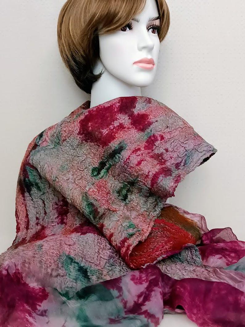 May include: A textured felted scarf featuring a mottled pattern of deep red, muted green, and grey tones. The scarf has a thick, uneven surface texture and is layered over a sheer, lightweight fabric with a matching dark pink and green abstract print.