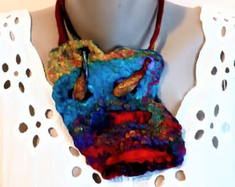 May include: A colorful, abstract felt necklace with a blue, red, and yellow color scheme. The necklace is made of felted wool and has a unique, organic shape.