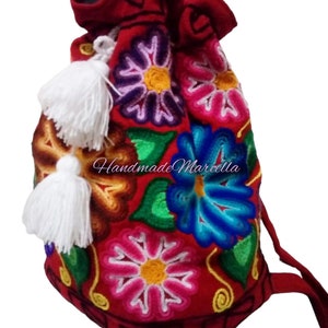 May include: Red drawstring bag with embroidered flowers in various colors, including pink, blue, green, and yellow. The bag has white tassels and the text "Handmade Marcella" is embroidered on the front.