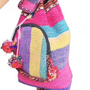 May include: A handmade, colorful backpack with a striped design in pink, purple, yellow, and blue. The backpack features a small zippered pocket, decorative pom-poms, and the text "Handmade Marcella".