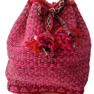 May include: A pink woven drawstring bag with a red and brown patterned strap and tassels. The bag has a red and white border.
