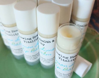 May include: A close-up of a group of white tubes with labels that say "Renewing Health & Vitality" and "Lemon Balm Lip Balm". The tubes are arranged in a circle on a green surface.