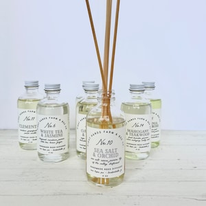 May include: A collection of eight glass bottles with white labels and black text. The bottles contain reed diffusers with various scents, including Sea Salt & Orchid, White Tea & Jasmine, and Mahogany & Teakwood. Each bottle is 4 oz and features a handwritten label with the scent name and number.