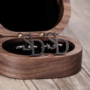 May include: A pair of black metal cufflinks with the letters "SD" engraved on them. The cufflinks are in a wooden box.