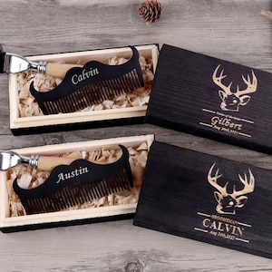 May include: A set of personalized grooming gifts. Each set includes a wooden mustache comb with a name engraved, a razor, and a wooden box with a deer head design. The boxes are black with gold lettering. The combs are black with a wooden handle.