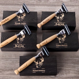 May include: Five personalized razors with wooden handles and silver blades are displayed on individual black boxes. Each razor handle is engraved with a name. The boxes feature a deer head logo and additional text.