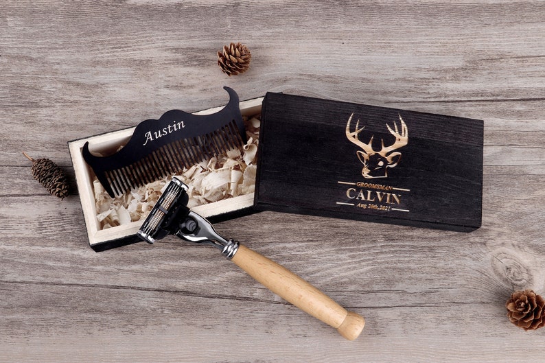 May include: A black wooden box with a deer head design and the name "Calvin" engraved on the lid. Inside, a black mustache comb with the name "Austin" and a razor with a wooden handle are visible.