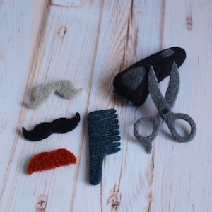 May include: A set of felt grooming tools for a pretend barbershop. The set includes a pair of scissors, a comb, a razor, and three different moustaches.