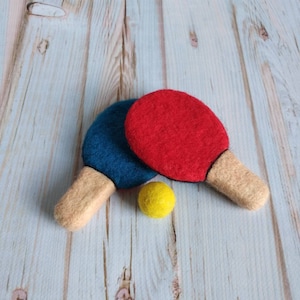 May include: Two felt ping pong paddles, one red and one blue, with a yellow felt ball. The paddles have beige handles.
