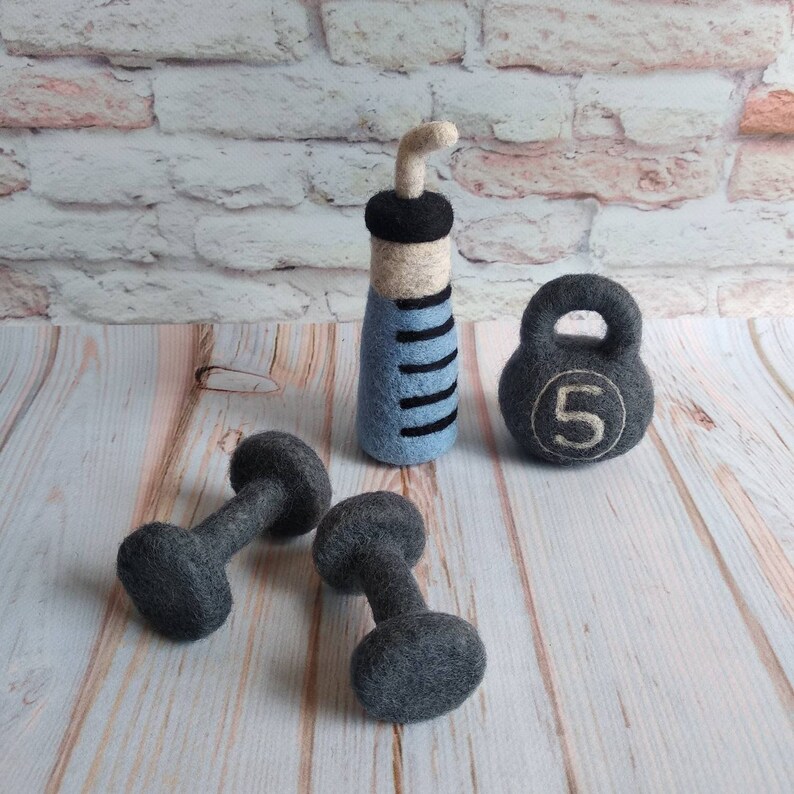 May include: A set of felt fitness equipment including a blue and white water bottle, a gray kettlebell with the number 5 on it, and two gray dumbbells.