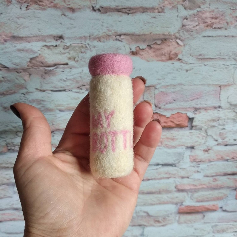 May include: A white felt baby bottle with a pink felt top and the words "My Bottle" written in pink felt.