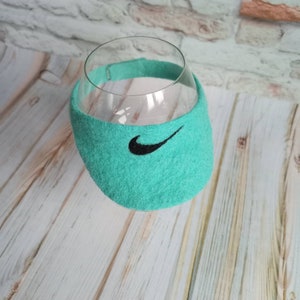 K&ouml;nnte beinhalten: Ein t&uuml;rkisfarbener Weinglas&uuml;berzug aus Filz mit einem schwarzen Nike-Swoosh-Logo.