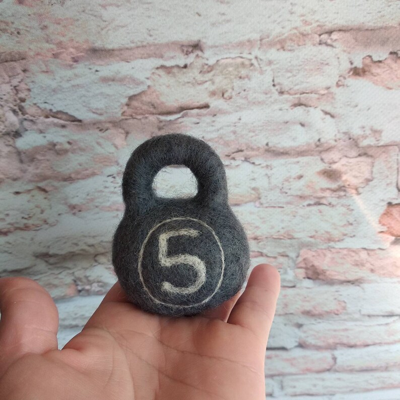 May include: A gray felt kettlebell with a white felt number 5 on the front.