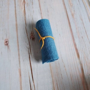 May include: A roll of teal blue felt fabric tied with a yellow string.