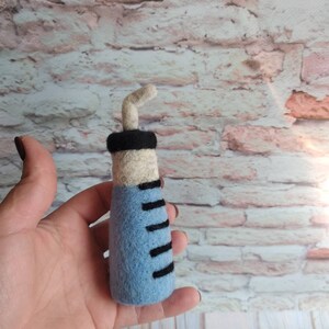 May include: A blue and white felt syringe with a black needle. The syringe has black markings on the side.