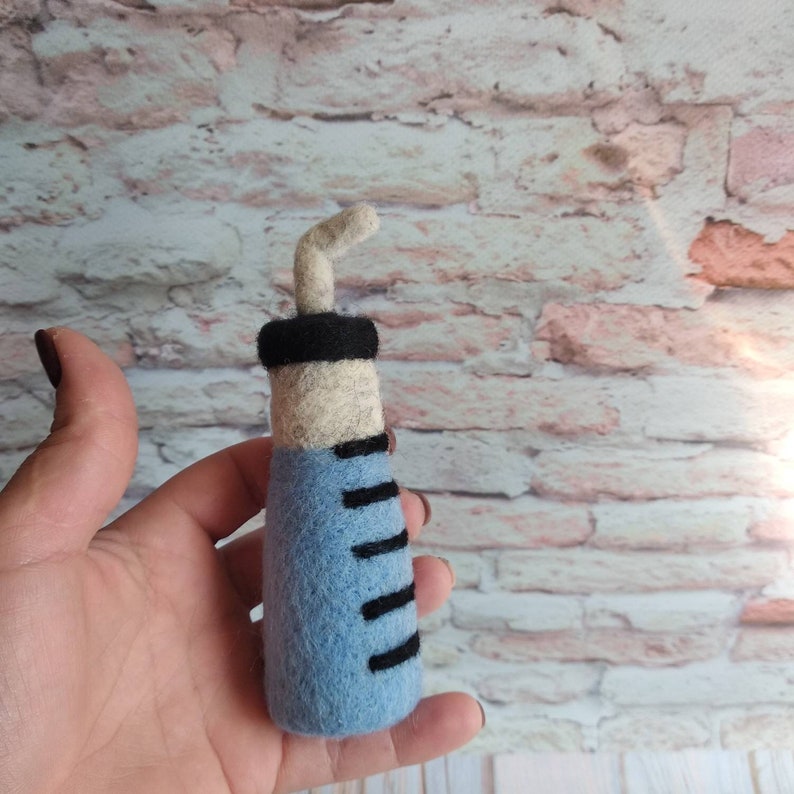 May include: A blue and white felt syringe with a black needle. The syringe has black markings on the side.