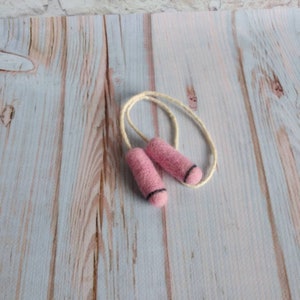 May include: A pink felt jump rope with white string. The jump rope is on a light wood background.